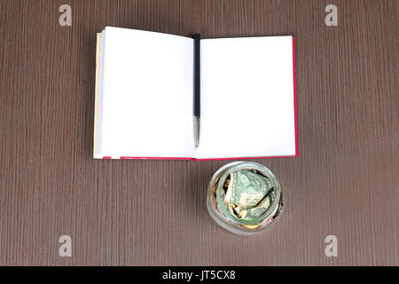 Glas mit Geld zu sparen, und öffnen Sie das Notebook auf hölzernen Tisch öffnen Stockfoto