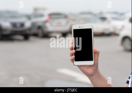Frau hand Smartphone mit leeren Bildschirm auf verschwommenen Hintergrund der Parkplatz. mein Auto mittels Anwendung Telefon Konzept Stockfoto