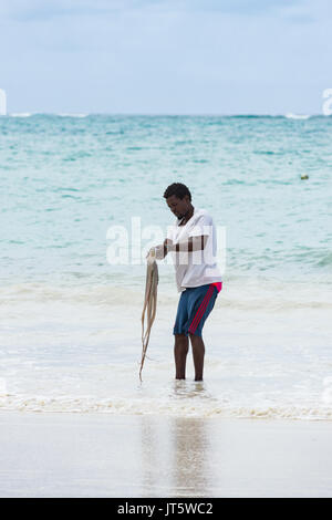 Fischer wäscht gefangen Octopus in Meerwasser durch Shoreline Beach, Diani, Kenia Stockfoto