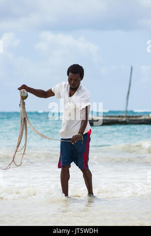 Fischer wäscht gefangen Octopus in Meerwasser durch Shoreline Beach, Diani, Kenia Stockfoto