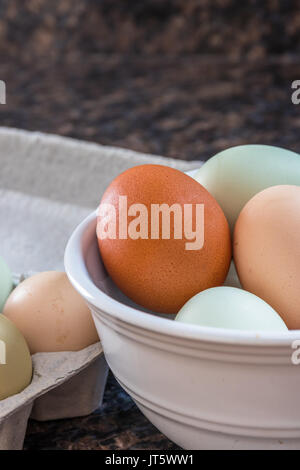Vertikale Nahaufnahme Foto von bunten Eier in einer weißen Schüssel auf eine Küchentheke mit mehr Eier in einem grauen Karton auf der Seite Stockfoto