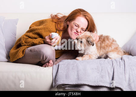 Wunderschöne, rothaarige Frau mit Orange Pullover sitzt mit ihrem Hund Stockfoto