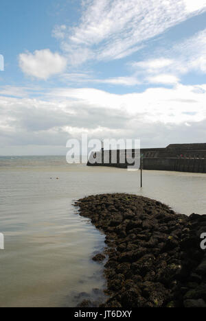 Der Wellenbrecher in Porthcawl, Wales, im Vordergrund mit der hafenmauer und Leuchtturm im Hintergrund Stockfoto