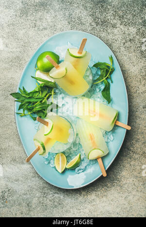 Erfrischende Limonade im Sommer Eis am Stiel mit Limette und Minze in Gläsern mit Spänen zerkleinert Eis auf blauen Platte über grauer Hintergrund, Ansicht von oben Stockfoto