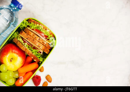 Gesunde Schule Lunch Box mit Sandwich, Apfel, Weintrauben, Möhren und eine Flasche Wasser in der Nähe von weißen Holz- Hintergrund. Stockfoto