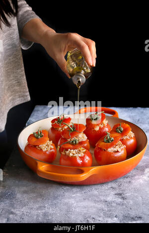 Weibliche Hand gießen Olivenöl gefüllte Tomaten mit Hackfleisch und Reis Stockfoto