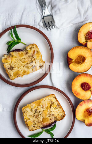 Pfirsich Brot serviert auf zwei weiße Platten auf einem weißen Hintergrund durch halbierte Pfirsiche aus der Ansicht von oben fotografiert begleitet. Stockfoto