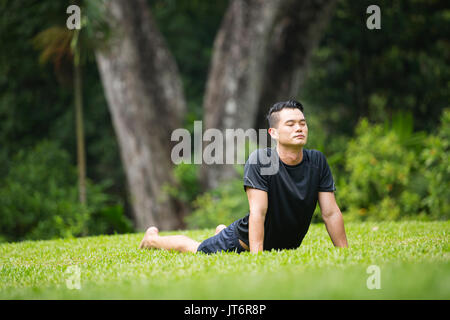 Asiatischer mann Üben Yoga in einem Garten. gesunder Lebensstil und Entspannung Stockfoto