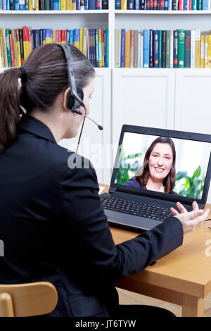 Leiter der Abteilung Human Resources mit Headset und Computer in Ihrem Büro, die Durchführung einer Videokonferenz Job Interview mit einem jungen Bewerberin Stockfoto