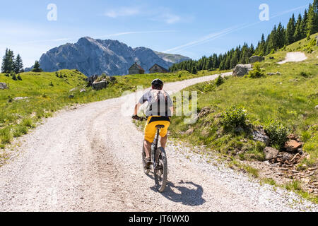 Mountainbiker auf einer Schotterstraße am Nassfeld in der Karnischen Alpen mit Blick auf die Berge Rosskofel Stockfoto