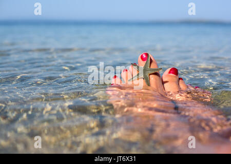 Weibliche Füße mit Seestern auf dem Wasser Stockfoto