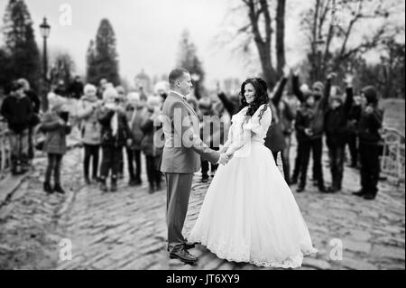 Wunderschöne Hochzeit Paar, Hände auf dem Bürgersteig während die Masse der Kinder nimmt Bilder von Ihnen. Schwarz-weiß Foto. Stockfoto