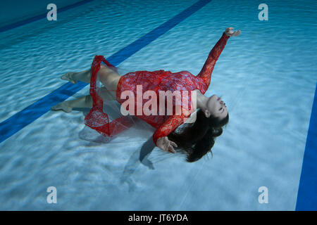 Schwimmer in einem roten Kleid stellt unter Wasser zeigen Zahlen. Stockfoto