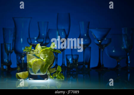 Cocktail mit Kalk, Eis und Pfefferminze Blätter auf einem Glastisch in bar. blauen Hintergrund. Stockfoto