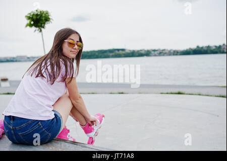 Porträt von einem schönen Mädchen mit Sonnenbrille, T-Shirt und Shorts setzen auf rollerblades Outdoor neben dem See. Stockfoto