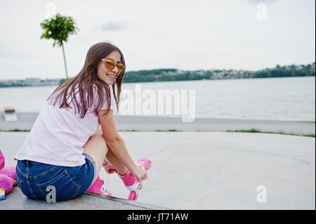 Porträt von einem schönen Mädchen mit Sonnenbrille, T-Shirt und Shorts setzen auf rollerblades Outdoor neben dem See. Stockfoto