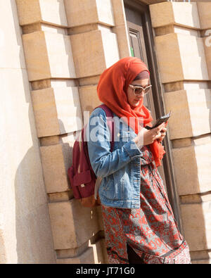 Junge muslimische Frau, tragen bunte Kopftuch und Minirock und Jeansjacke mit Handy in York, England Stockfoto