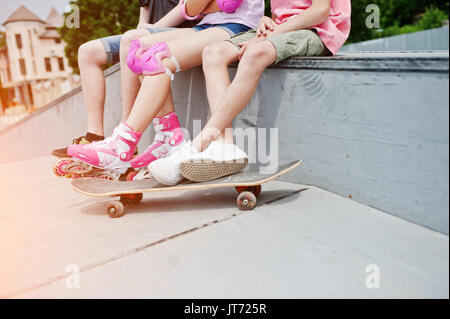 Nahaufnahme der männlichen Beine auf Skateboard und weibliche Beine in Inline-skates und Schutz. Stockfoto