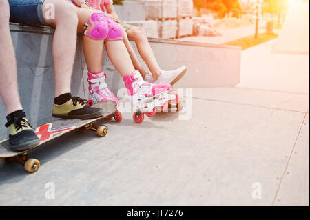 Nahaufnahme der männlichen Beine auf Skateboard und weibliche Beine in Inline-skates und Schutz. Stockfoto