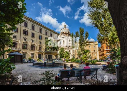 Kleine Piazza in Rom Italien als Damen auf einer Parkbank im Schatten mit einer Kirche Dom im Hintergrund an einem sonnigen Tag entspannen Stockfoto