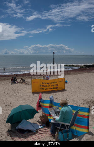 Ältere Dame liest eine Zeitung auf dem Strand bei Brüder Cliff, Christchurch, Dorset, Großbritannien Stockfoto