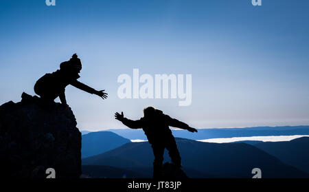 Wandern Paar in Silhouetten, die sich gegenseitig helfen für Erfolg Stockfoto