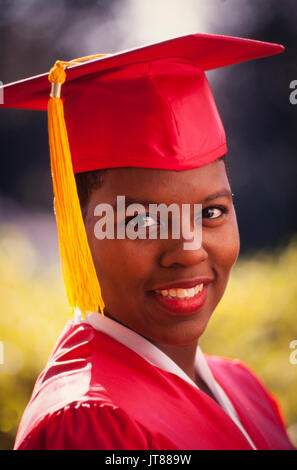 Einen afrikanischen amerikanischen Hochschulabschluss in ihrem roten Kappe und Kleid mit einem gold Quaste. Stockfoto