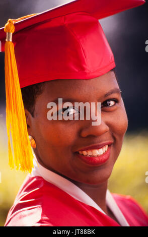 Einen afrikanischen amerikanischen Hochschulabschluss in ihrem roten Kappe und Kleid mit einem gold Quaste. Stockfoto