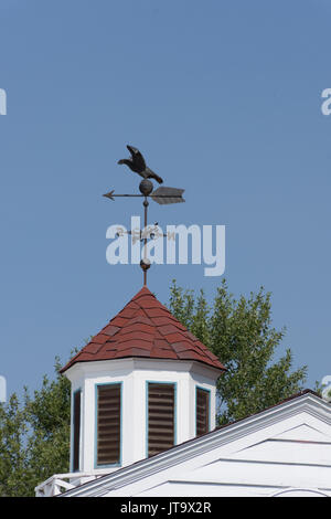 Ein Black Metal Wetterfahne mit einem fliegenden Vogel auf einem Turm mit rotem Dach. Der Turm befindet sich auf einem ländlichen Scheune. Stockfoto