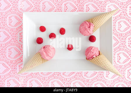 Schaufeln des hausgemachten Himbeer Eis in der Waffel mit frischen Himbeeren auf einem weißen Porzellanteller und Rosa geschnürt Hintergrund angeordnet. Stockfoto