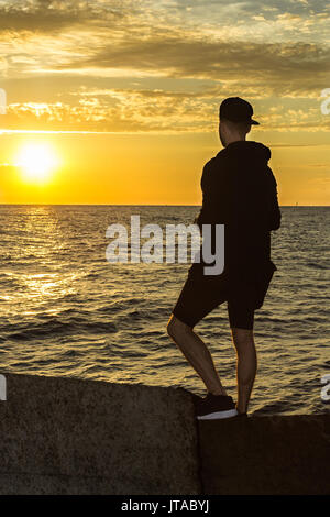 Ein junger Mann steht an der Ostsee und Suchen am Sonnenuntergang Stockfoto