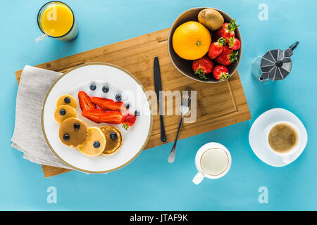 Blick von oben auf die Pfannkuchen mit Beeren auf Küche Schreibtisch mit Kaffee und Orangensaft Stockfoto