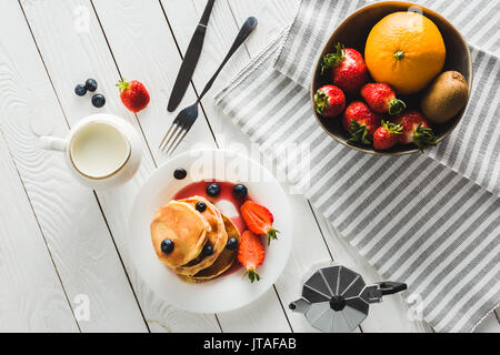 Blick von oben auf die hausgemachten süßen Pfannkuchen und verschiedene Früchte für gesundes Frühstück auf hölzernen Tischplatte Stockfoto