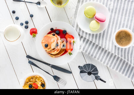 Blick von oben auf die Pfannkuchen mit Macarons und Kaffee mit corn flakes auf hölzernen Tischplatte Stockfoto