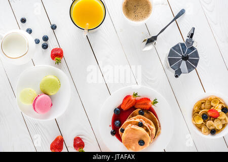 Blick von oben auf die Pfannkuchen mit Macarons und Kaffee mit corn flakes auf hölzernen Tischplatte Stockfoto