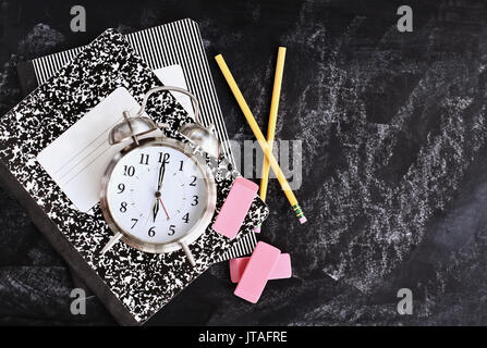 Zurück in der Schule liefert. Bücher, Wecker, Radiergummis und Bleistifte über eine Tafel oder Tafel mit Platz für Textfreiraum. Stockfoto