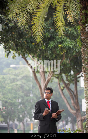 Indische Geschäftsmann mit seinem Smart Phone im Freien in einer asiatischen Stadt. Stockfoto