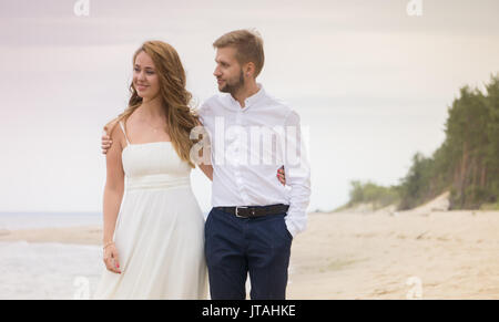 Junge glücklich verheiratetes Paar gehen Hand in Hand am Strand entlang dem Meer im Sommer Abend Stockfoto