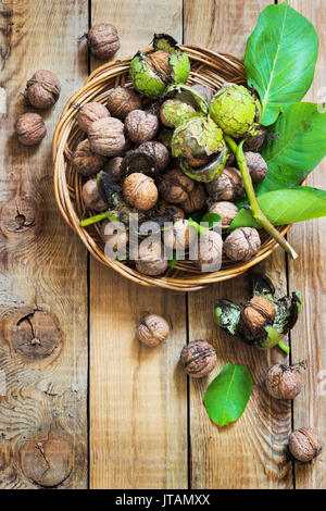 Walnüsse in der grünen Schalen mit Blättern, die auf einer hölzernen Hintergrund Stockfoto