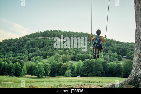 Eine weibliche Wanderer ist auf einer Schaukel im Wald mit Blick auf die Berge. Stockfoto