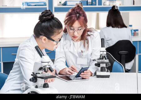 Wissenschaftler gemeinsam mit Mikroskopen und Smartphone im chemischen Labor, Wissenschaftler team konzept Stockfoto