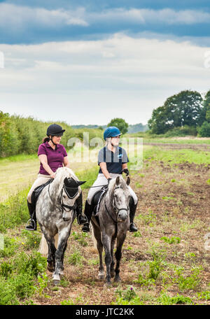 Zwei junge Mädchen aus reiten Pferde auf einem späten Sommer am Nachmittag Stockfoto