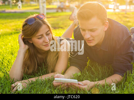 Sonnigen Porträt süßen jungen Paares liegen entspannen auf dem Rasen zusammen hört Musik im Kopfhörer auf Smartphone, Sommertag. Stockfoto