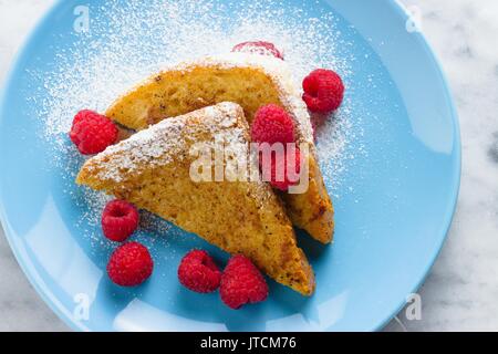 Top down Sicht auf zwei french toast Dreiecke mit Zucker und Himbeeren auf blauen Platte Stockfoto