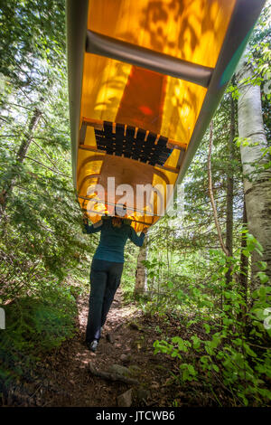 Eine weibliche Paddler portagen Ihr Kanu über einen Trail in der Boundary Waters Canoe Area Wilderness (BWCAW). Stockfoto