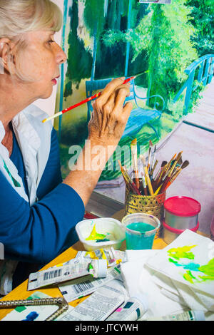 Blond, Pony-tailed Senior Professional arbeiten auf eine Leinwand, auf der Basis einer Foto sie in Giverny, Frankreich nahm, auf dem Anwesen von Claude Monet. (Ar Stockfoto