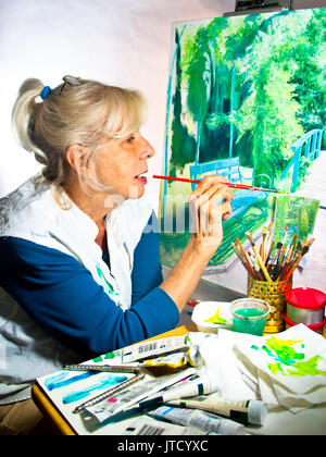 Blond, Pony-tailed Senior Professional arbeiten auf eine Leinwand, auf der Basis einer Foto sie in Giverny, Frankreich nahm, auf dem Anwesen von Claude Monet. (Ar Stockfoto