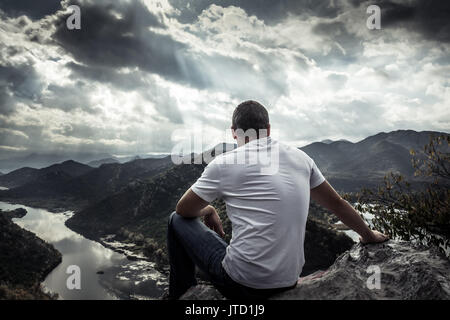 Einsamer Mann sucht mit der Hoffnung am Horizont auf Berggipfel mit dramatischen Sonnenlicht bei Sonnenuntergang mit Wirkung von Licht am Ende des Tunnels Stockfoto