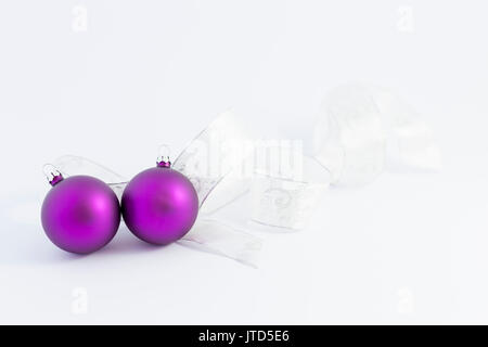 Schöne glänzende lila Weihnachtskugeln mit Weiß und Silber Farbband auf weißem Hintergrund Stockfoto