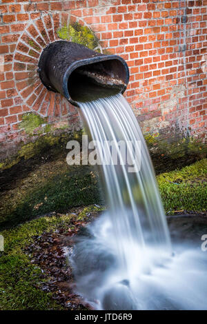 Wasser cascading aus Metall Rohr in der Wand auf grünem Moos montiert Stockfoto